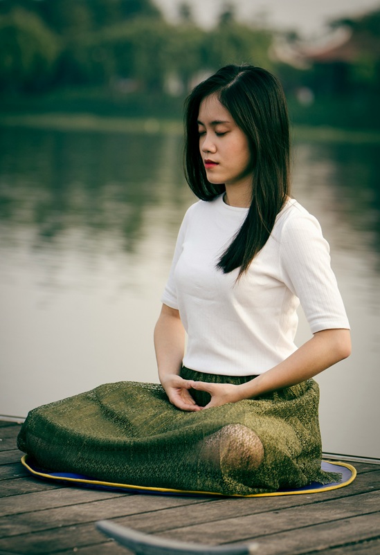 Woman meditating peacefully by the lake, looking calm and serene